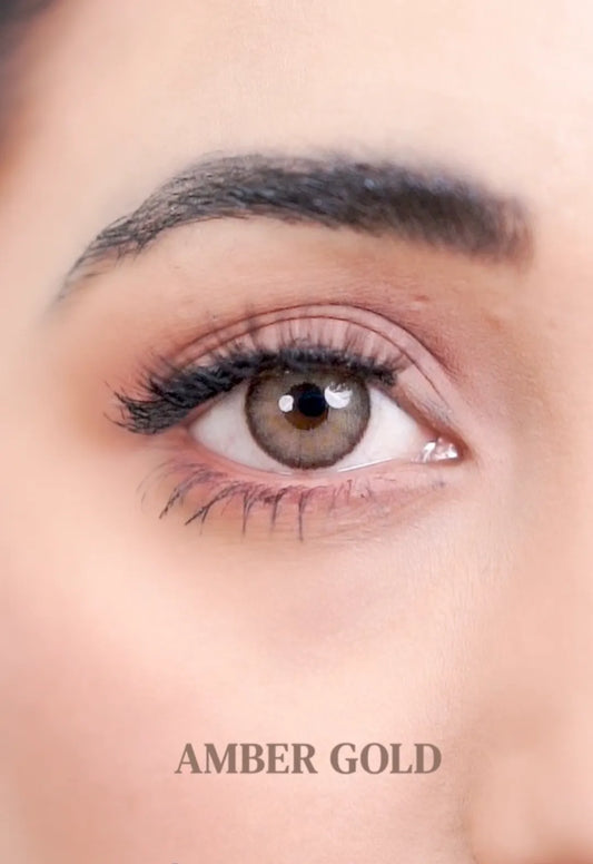 Close-up of a person's eye with brown ULTIMATE PLUS CONTACT LENSES and eyelashes, labeled 'AMBER GOLD'.