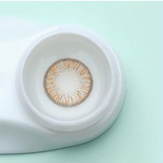 Brown contact lens in a white container on a light green background at best price online sale in Pakistan