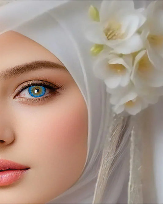 Close-up of a woman's eye with blue lenses a white hijab and a white flower in her hair.