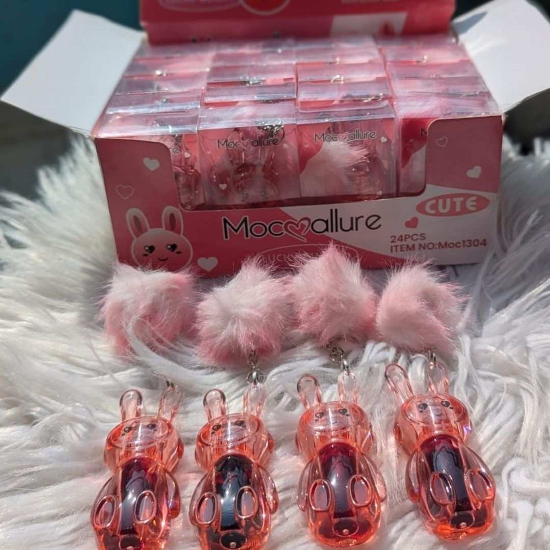 Pink bunny-shaped lip glows with fluffy tails on a white fur surface, in front of a pink box labelled 'Mocoallure'.