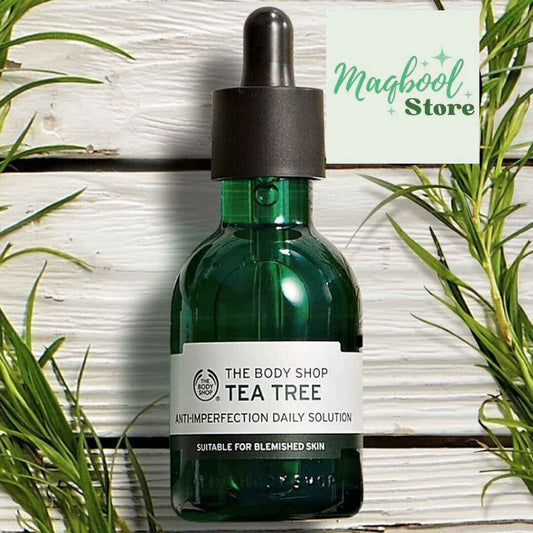 Green bottle of The Body Shop Tea Tree solution with a dropper on a wooden surface with plants.
#MaqboolStoreOfficial #maqboolstore