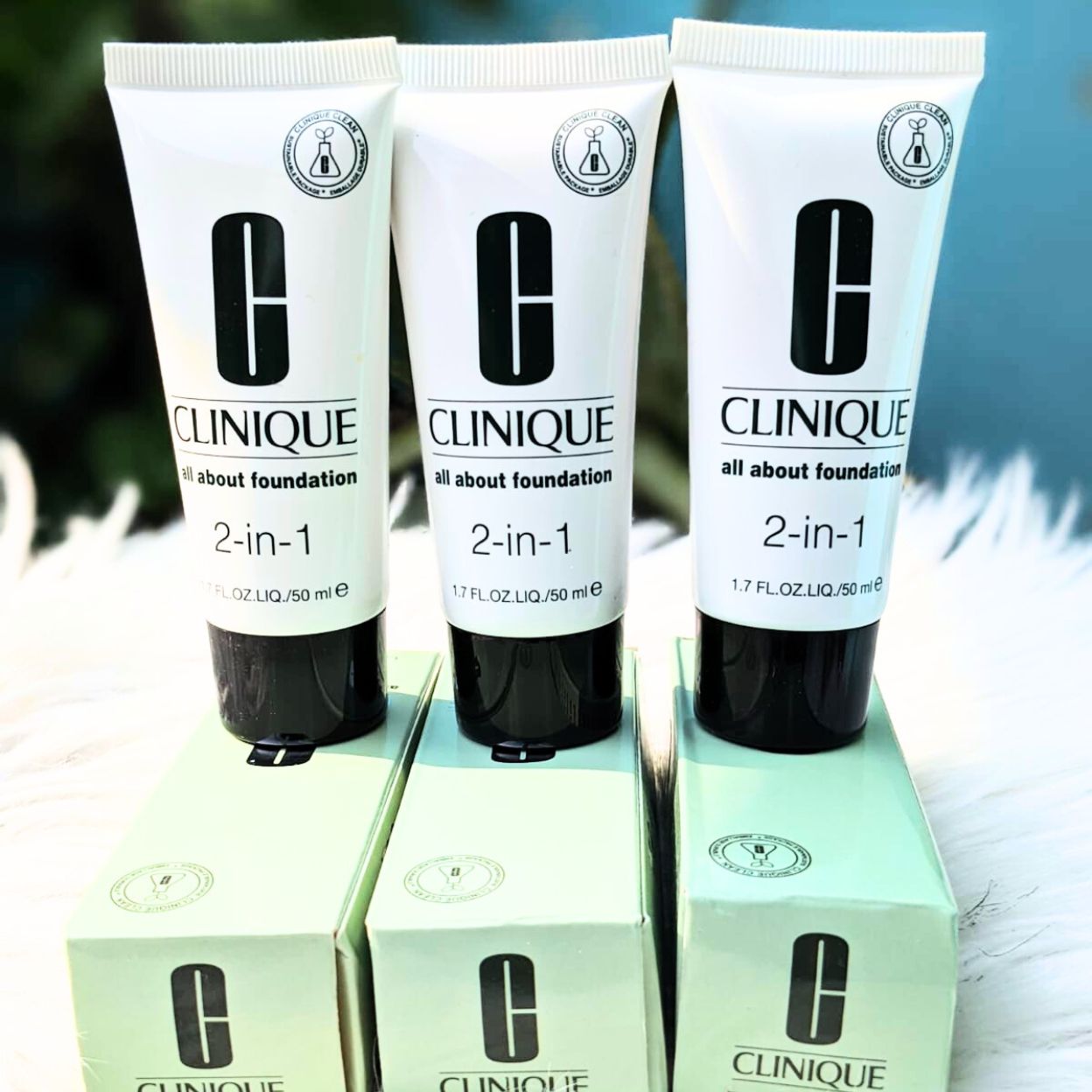 Three Clinique 2-in-1 foundation tubes on their boxes with a blurred natural background.