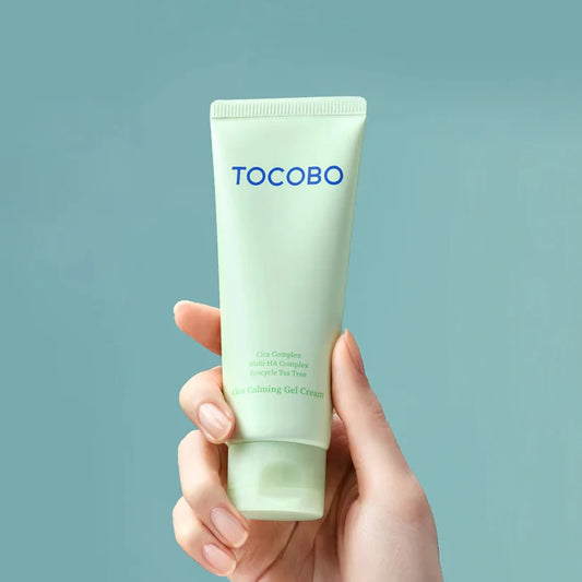 Hand holding a green tube of Tocobo-cica-calming-gel-cream-75ml-Maqboolstore against a light blue background