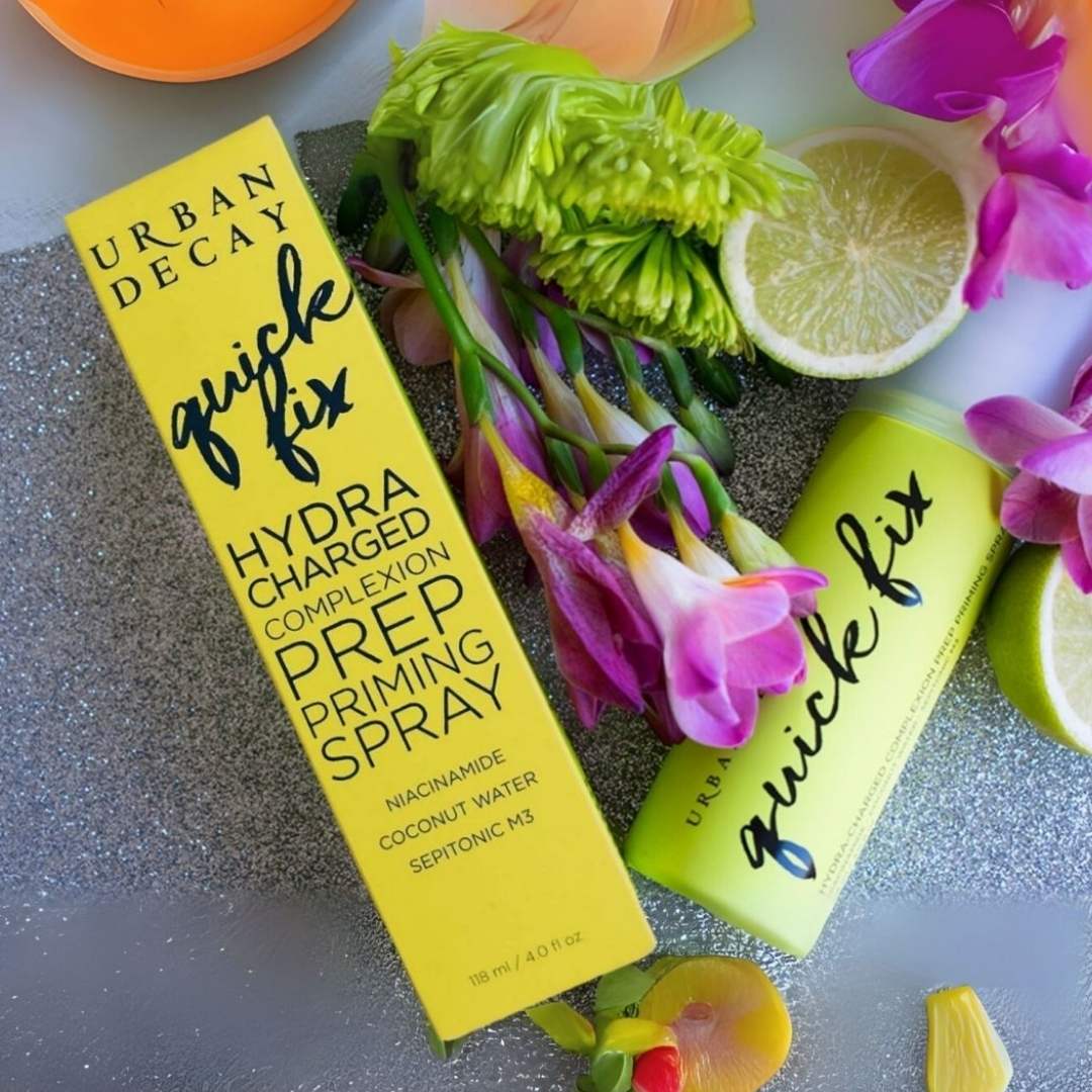 Urban Decay Quick Fix Hydra Charged Complexion Prep Priming Spray with packaging and flowers on a textured surface at best price online sale in Pakistan