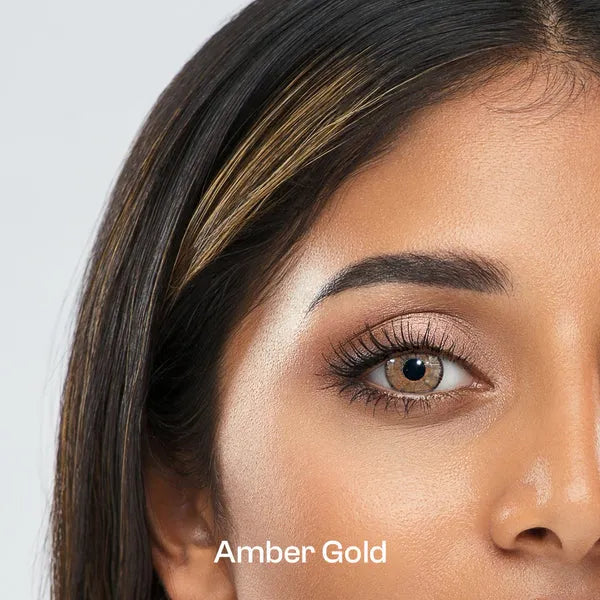 Close-up of a woman's face with ULTIMATE PLUS CONTACT LENSES 'Amber Gold' makeup on a light gray background