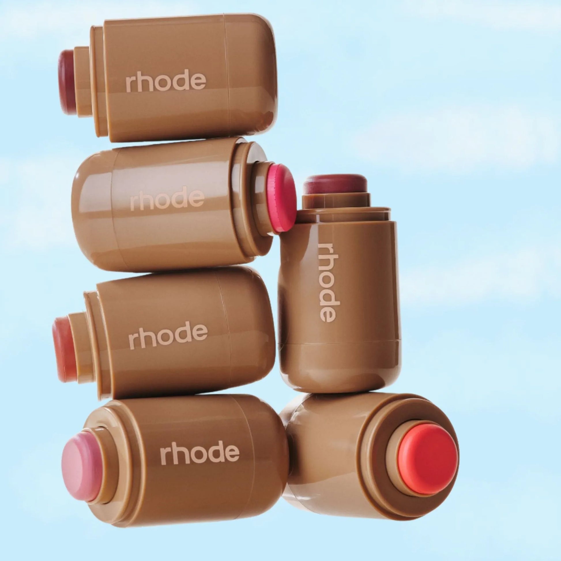 Stack of brown blush on Rhode containers with red caps on a light blue background
