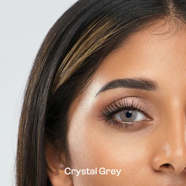Close-up of a woman's face with ULTIMATE PLUS CONTACT LENSES 'Crystal Grey' makeup on her eyelid against a light gray background.