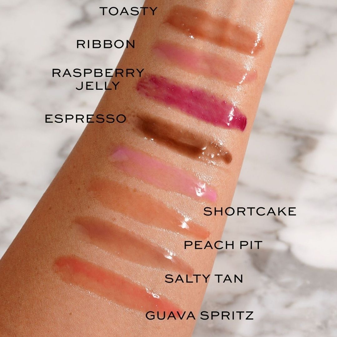 Lipstick swatches on a person's arm with labeled colors against a marble background
